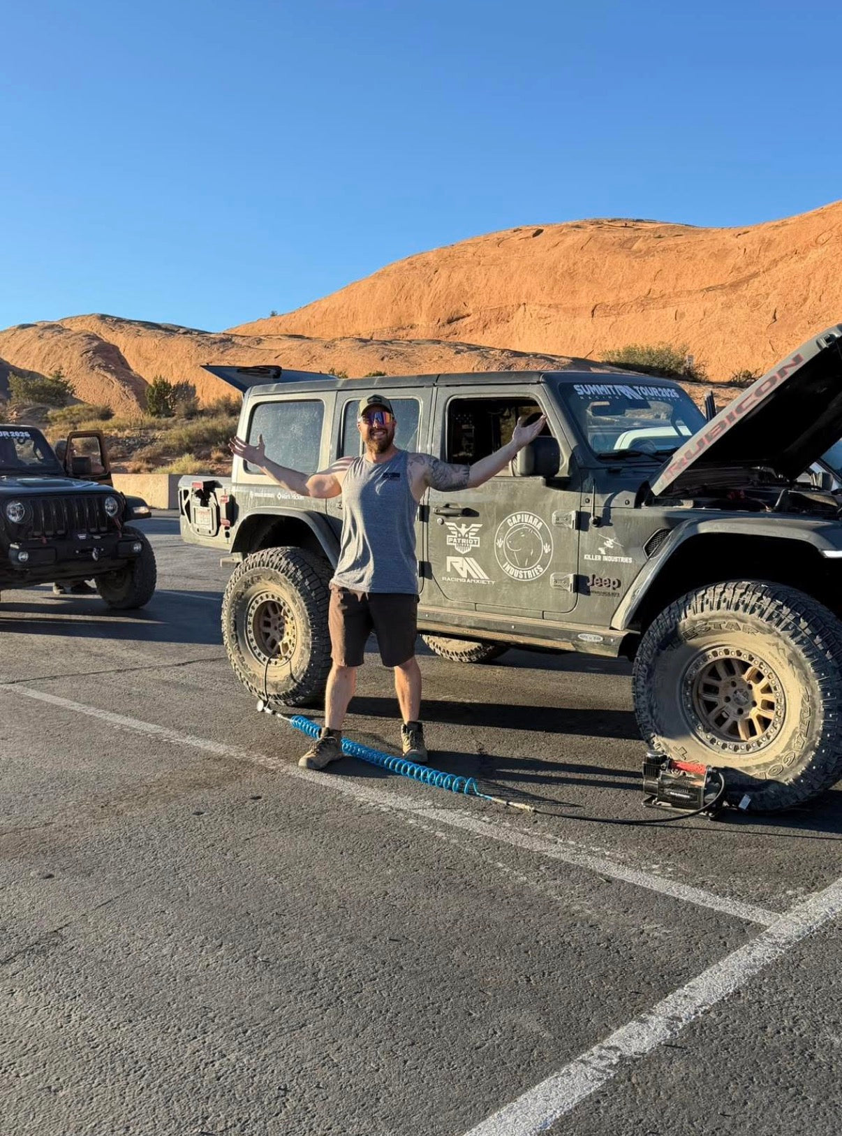 An off-road community member beside a Jeep in a red-rock landscape